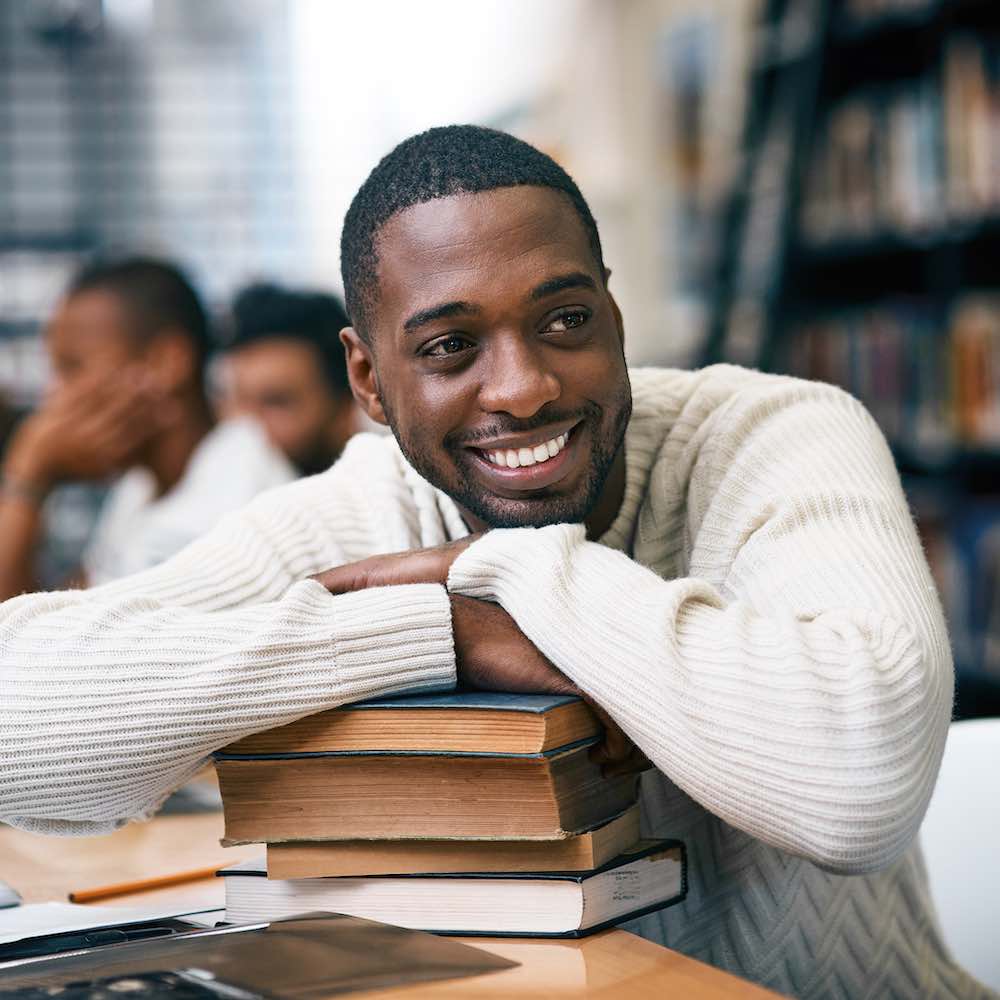 Man leaning on books in library smiling
